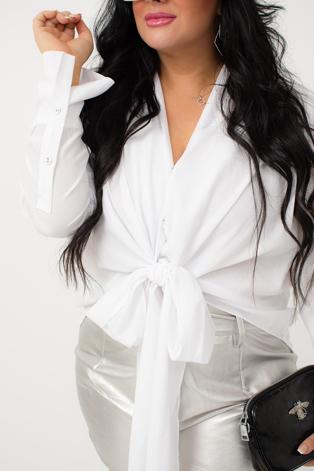 The White Bow Tie Blouse exudes elegance with its v neckline and long sleeves. The snap button front allows for easy wear, while the double button cuff closure adds a touch of sophistication. The high low hem creates a modern and stylish look. Perfect for a formal occasion or professional setting.